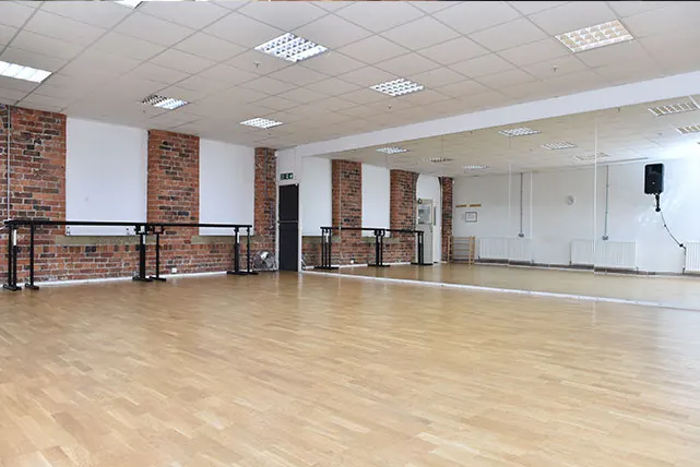 Empty dance studio with wooden floor, brick pillars, mirrored wall and ballet barre.