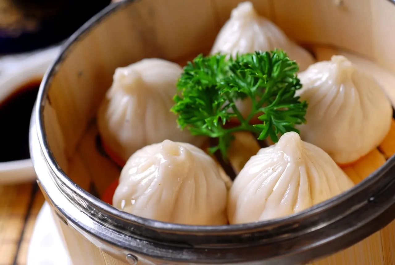 Steamed dumplings in a bamboo basket, garnished with fresh parsley and served with dipping sauce.