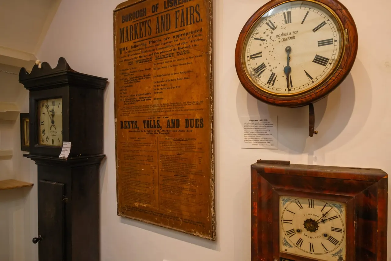 Historical wooden clocks and vintage signage displayed on a museum wall, including a tall case clock, wall-mounted round clock, and square wooden clock.