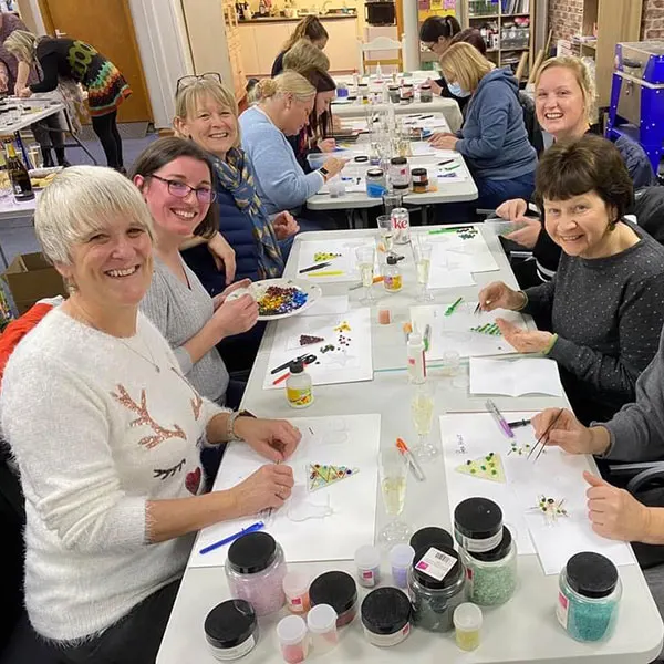 A group of people enjoying a painting workshop together at tables with art supplies and materials.
