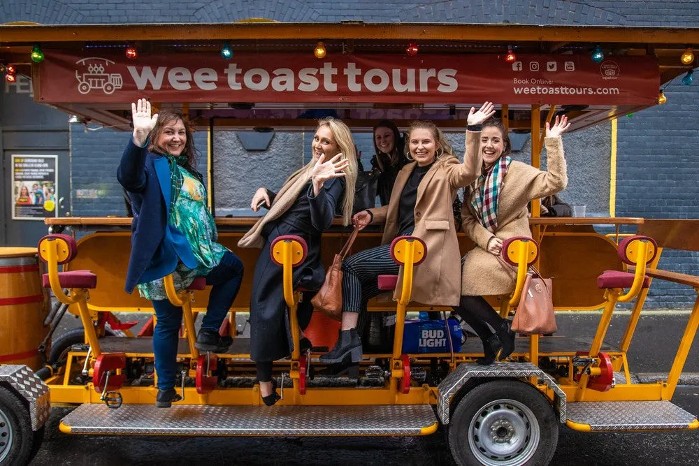 Five women wave and smile whilst seated on a yellow and red pedal-powered tour bus.