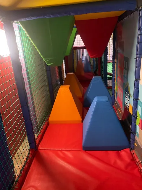 Colourful foam padded tunnel with stepping blocks inside a children's soft play area.