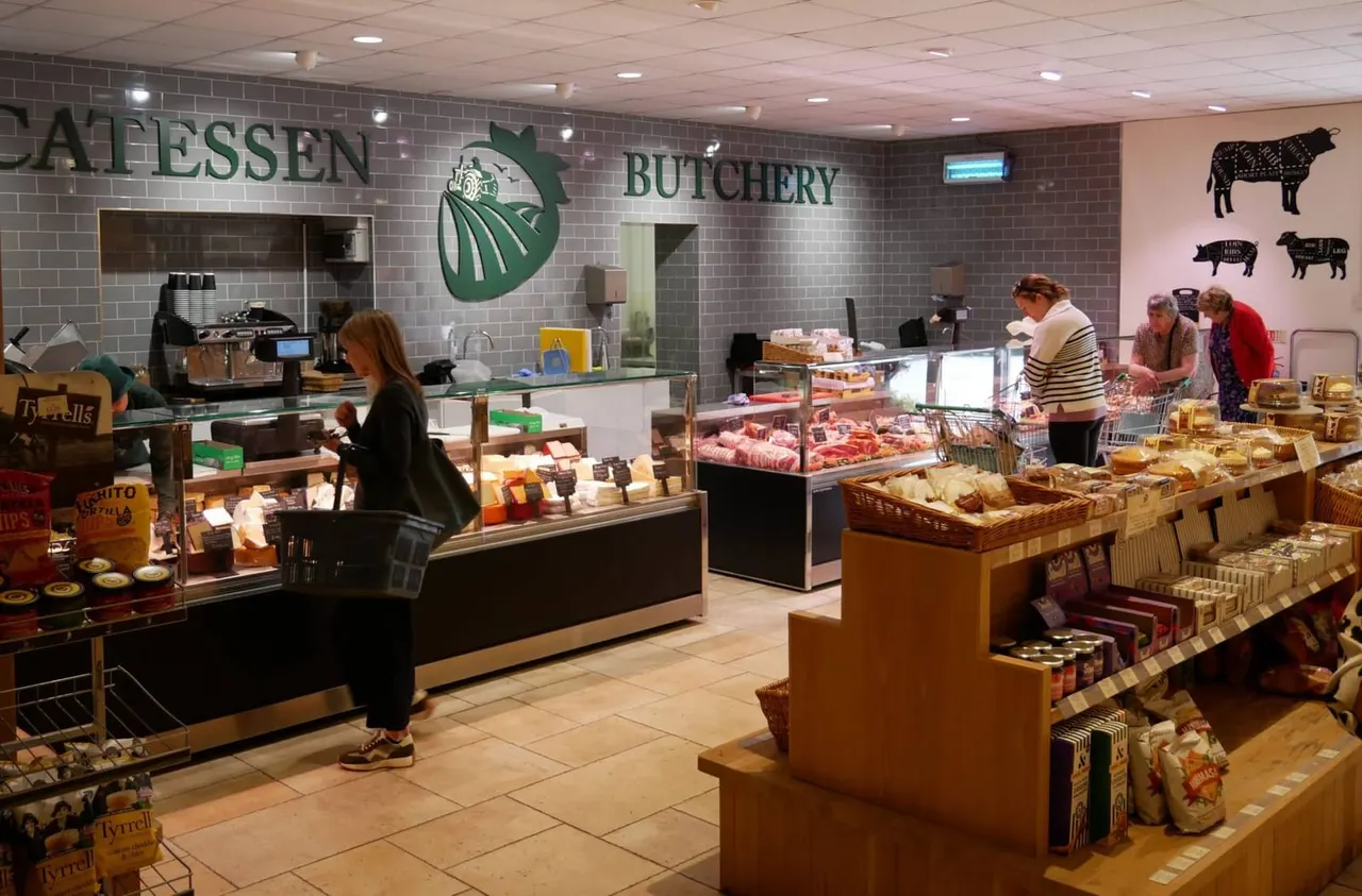 Interior of a butchery and farm shop with customers browsing meat counters and packaged products, staff behind service counter.