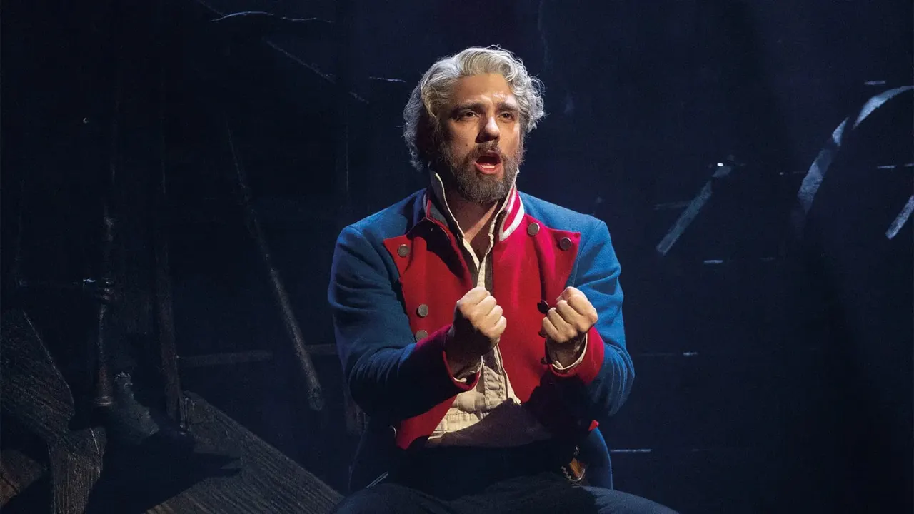 Actor in period costume performing on stage under spotlight.