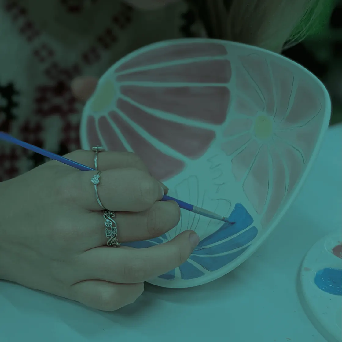 Child's hand painting a ceramic jellyfish dish with a blue brush at a pottery painting activity.