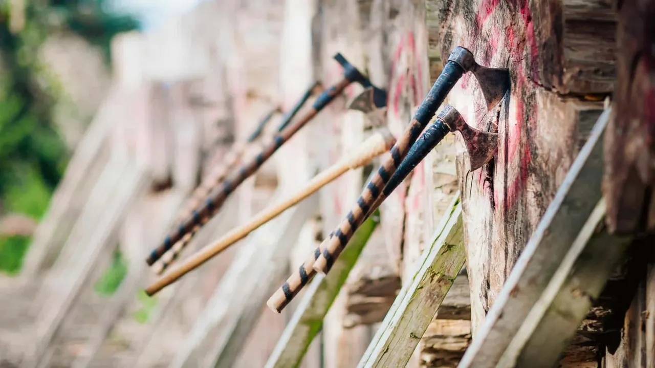 Axes leaning against a weathered brick wall with wooden beams, ready for axe-throwing.