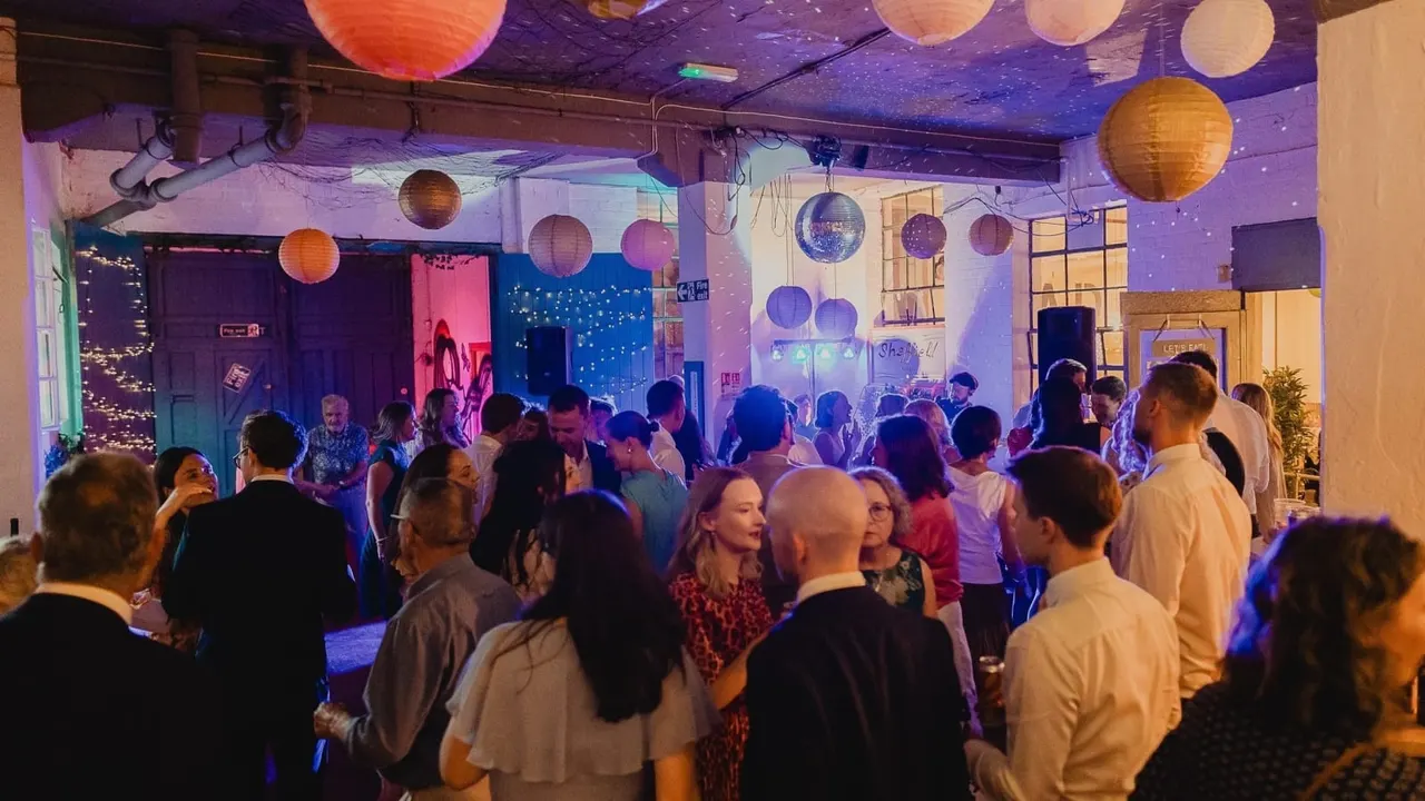 Crowded dance floor with guests under purple and blue lighting, colourful hanging lanterns and disco ball decorations.