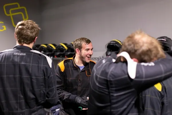 A group of people in black and yellow racing suits gather together indoors at a karting venue.