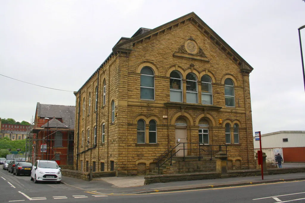 Historic Victorian stone building with arched windows on a street corner, parked cars nearby.