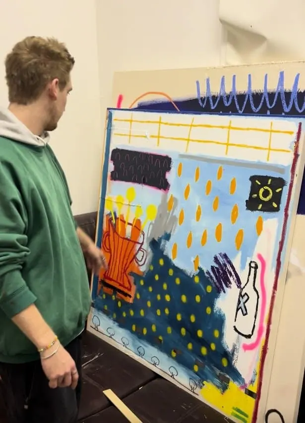 Person in green hoodie viewing a colourful abstract artwork with geometric shapes and weather-themed imagery on a gallery wall.