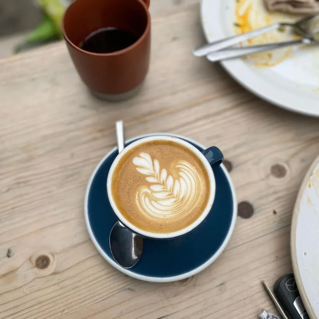 Cappuccino with latte art on a wooden table surrounded by plates and other drinks.