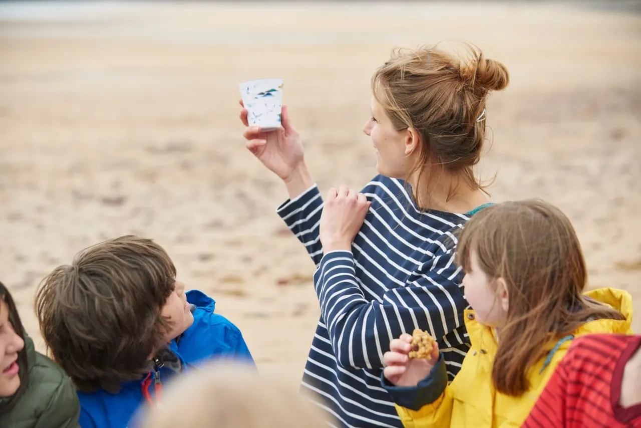Woman and children on a sandy beach examining a small container, possibly studying rock pooling specimens.