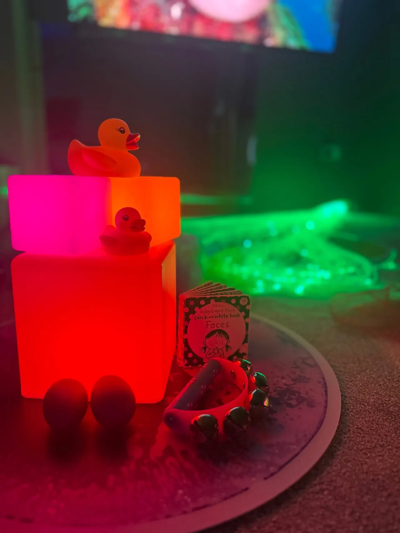Colourful neon-lit toys and sensory objects arranged on a mat in a bright, playful indoor play space for babies and toddlers.