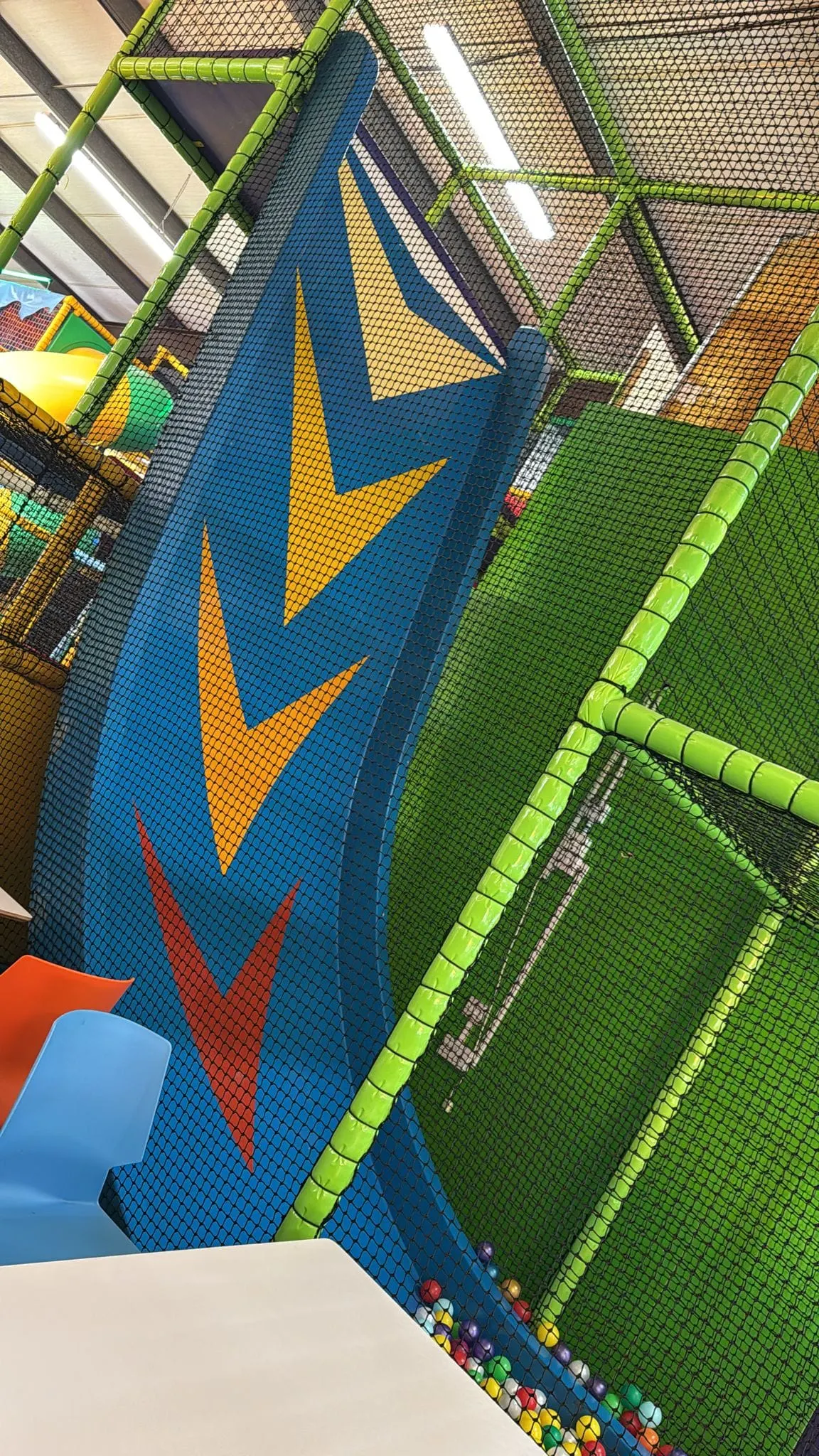 Indoor play area with colourful padded walls, netting, and green foam poles in a children's soft play facility.