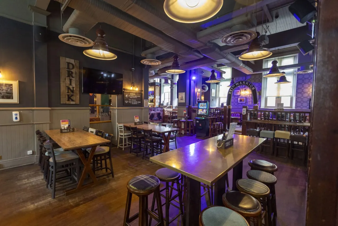 Interior of a pub with bar seating, wooden tables, purple lighting, and gaming machines.