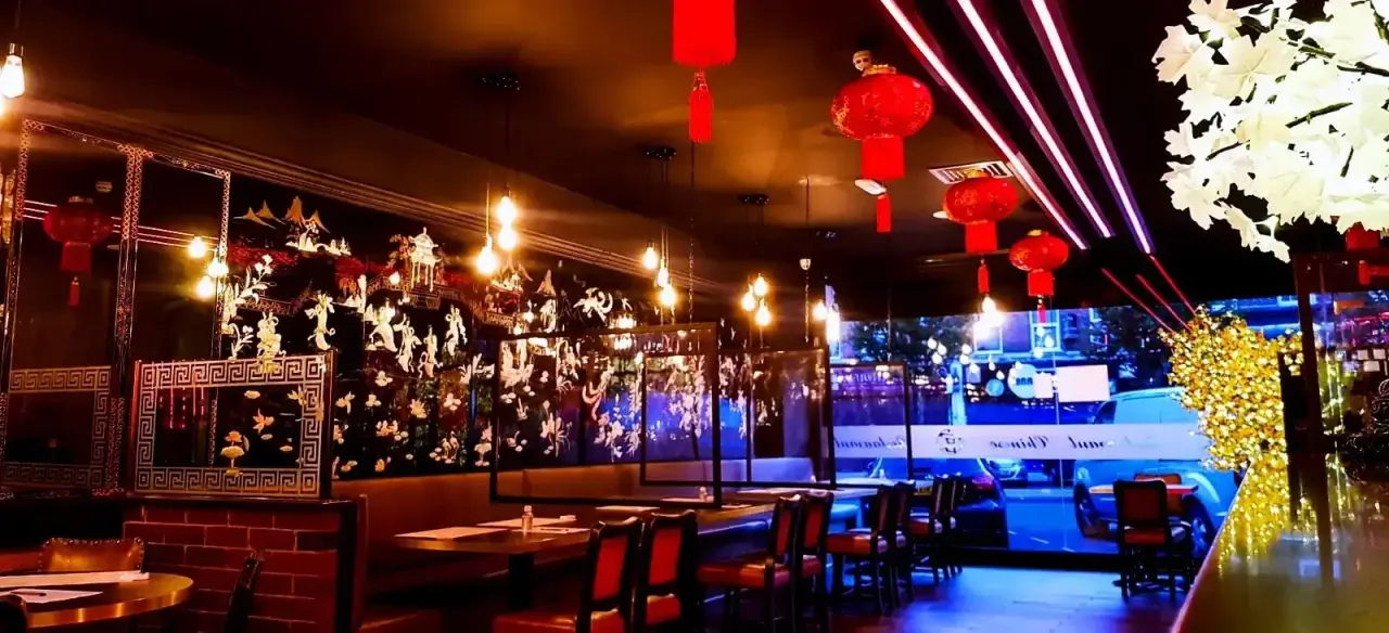 Elegant Asian restaurant interior with red lanterns, decorative panels and neon lighting overlooking a nighttime cityscape.