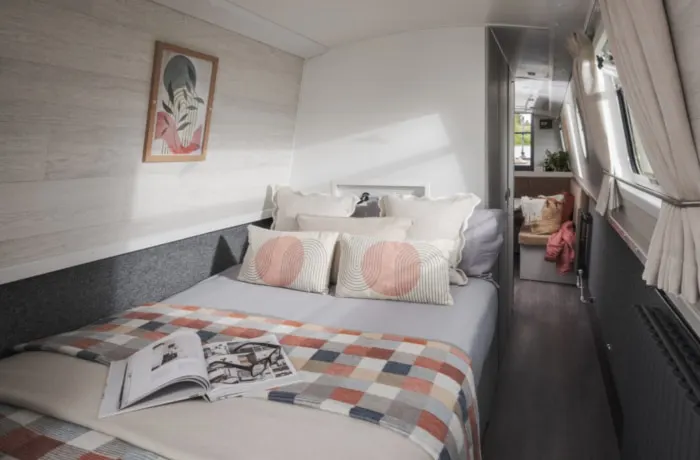 A narrow double bed with geometric patterned bedding and striped cushions inside a modern caravan bedroom.
