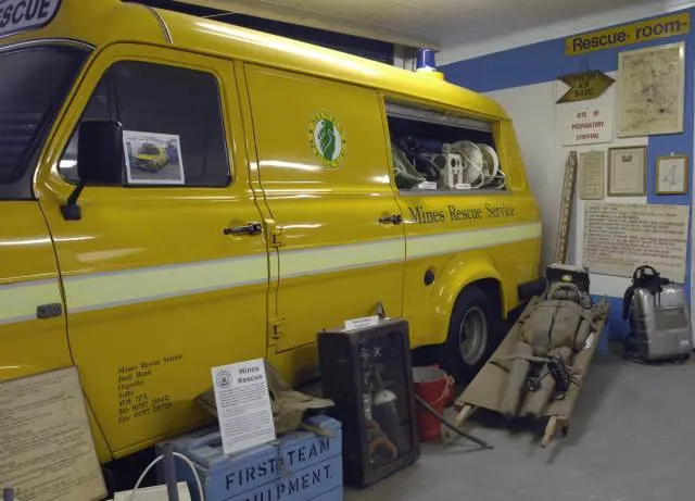 Yellow mountain rescue service van on display in indoor museum space with rescue equipment and information panels nearby.