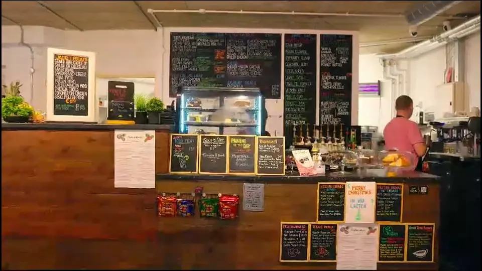 Staff member working behind counter at independent café with menu boards and display case.