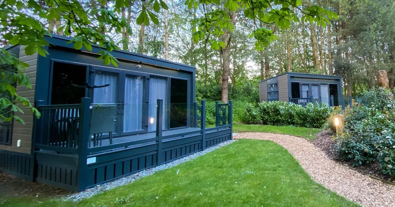 Modern lodge-style accommodation with decked veranda set among trees and manicured grounds at a caravan park.