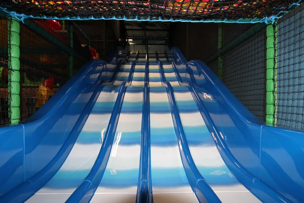 Multiple blue water slides with parallel lanes descending into an indoor play centre.