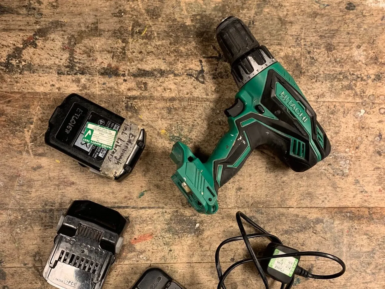 Overhead view of a green cordless drill with batteries and charger on a weathered wooden surface.