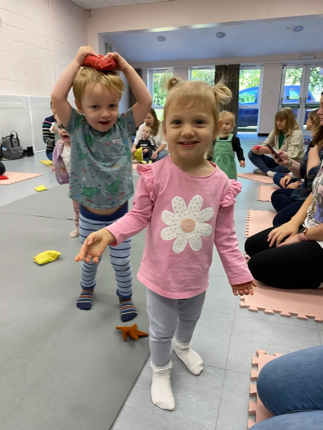 Young children playing with foam shapes on a padded floor in an indoor activity room.
