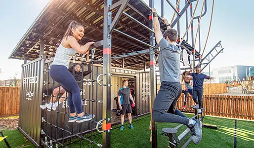 Group fitness class with people exercising on outdoor gym equipment in a rooftop facility.