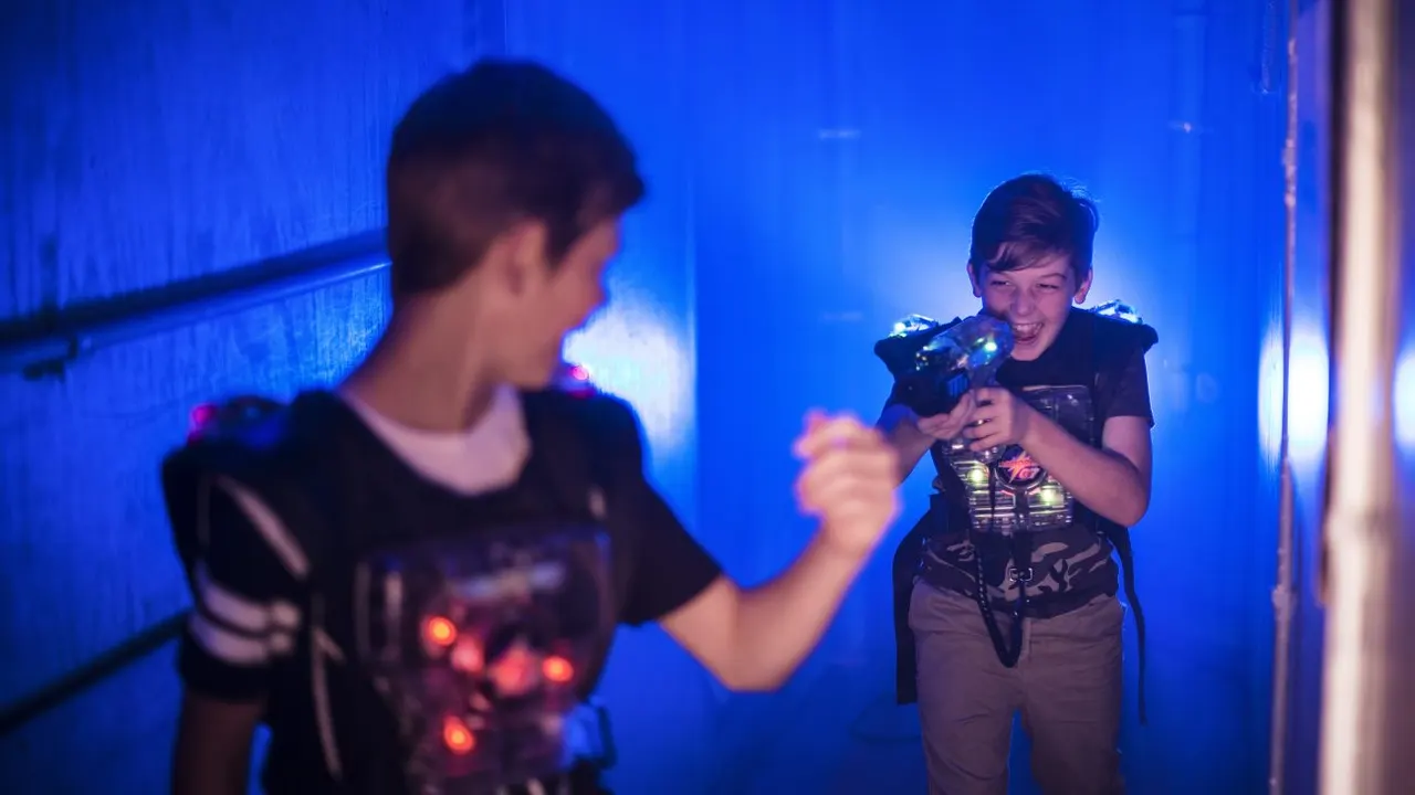 Two children playing laser tag in a dimly lit arena with blue lighting, holding laser guns.