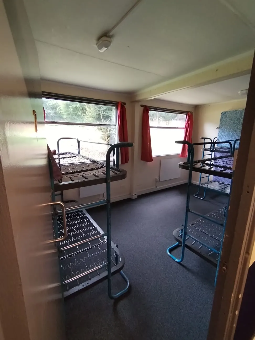 Interior of a hostel dormitory with multiple bunk beds and red-curtained windows.