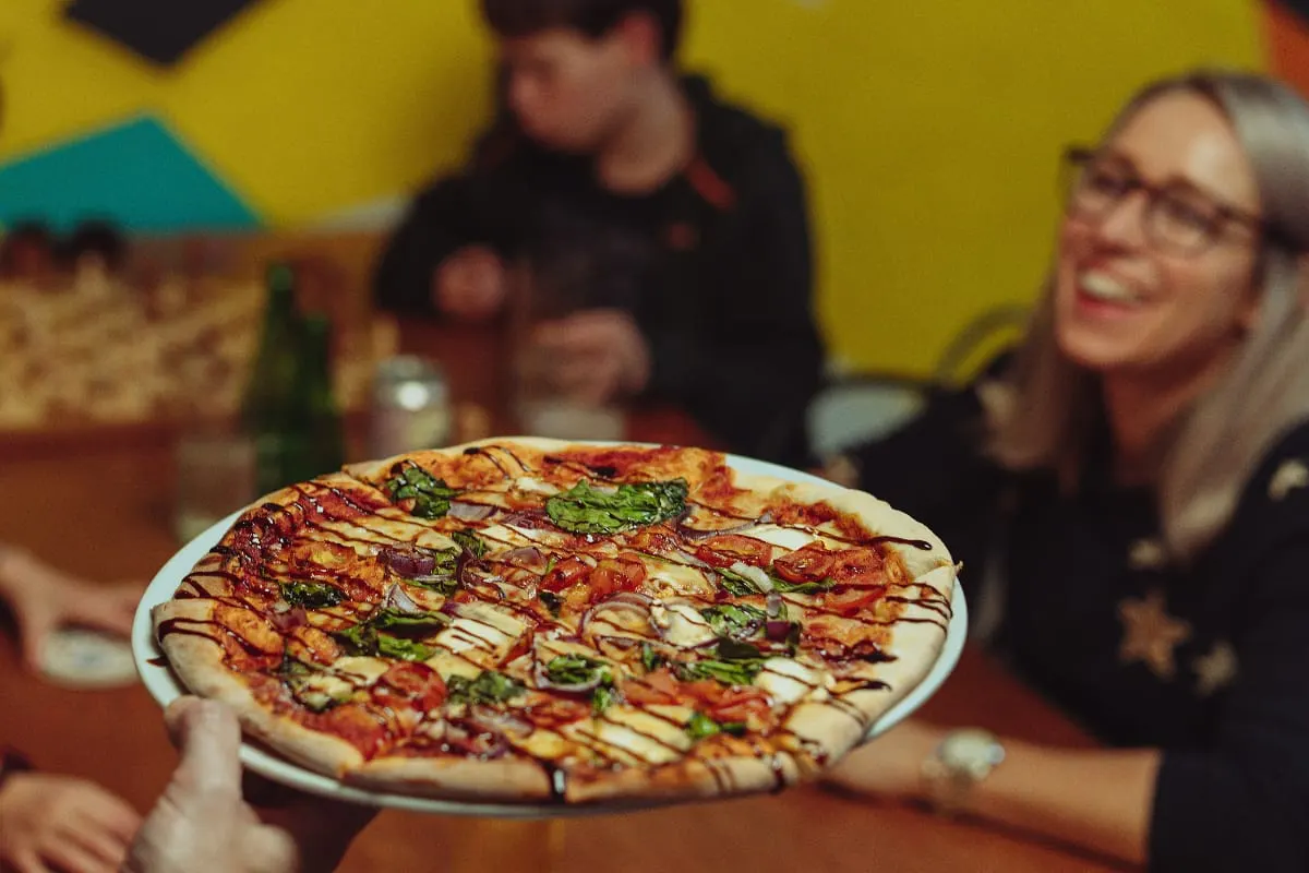 A freshly baked pizza with tomato sauce, cheese and greens is presented to guests in a colourful indoor venue.
