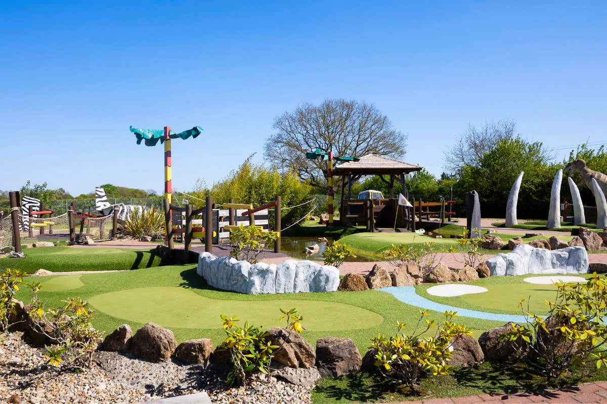 Themed mini golf course with colourful obstacles, white painted rocks, water features and jungle-style structures under clear blue sky.
