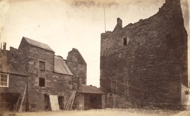 Historic stone castle ruins and associated buildings in a courtyard setting.