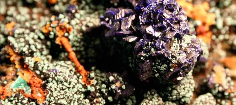 Close-up of colourful mineral specimens including purple, orange and pale green crystals on rock.