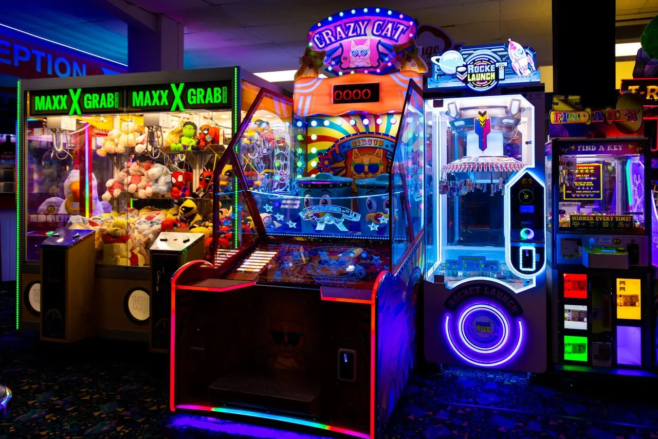 Brightly lit arcade games and prize machines with neon signs in an indoor entertainment venue.