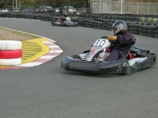 Kart racer in helmet and number 10 bib racing on indoor track past coloured barrier and bumper.