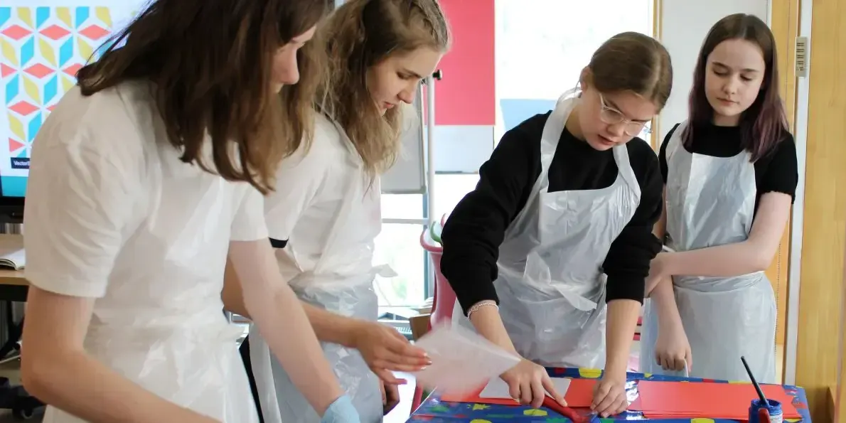 Four young people in aprons work together on a creative craft project at a table.