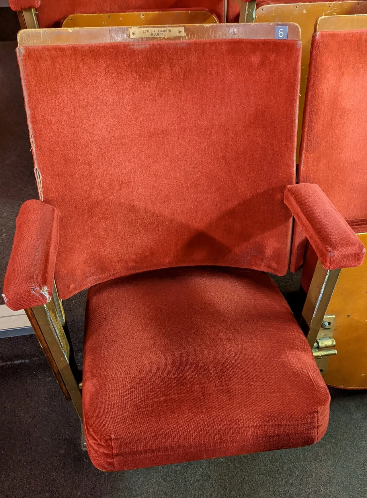 Vintage cinema seat upholstered in red fabric with wooden frame and brass fittings.