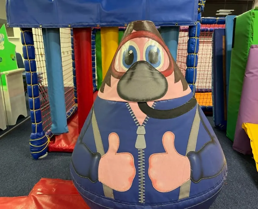 Colourful character-shaped play structure inside an indoor soft play area with padded climbing equipment.