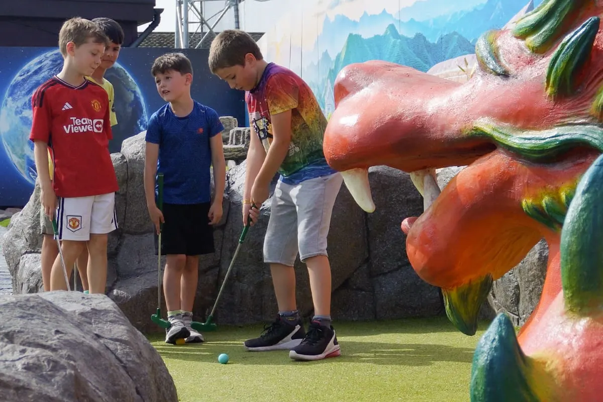 Children playing mini golf indoors with colourful fantasy-themed obstacles and backdrops.