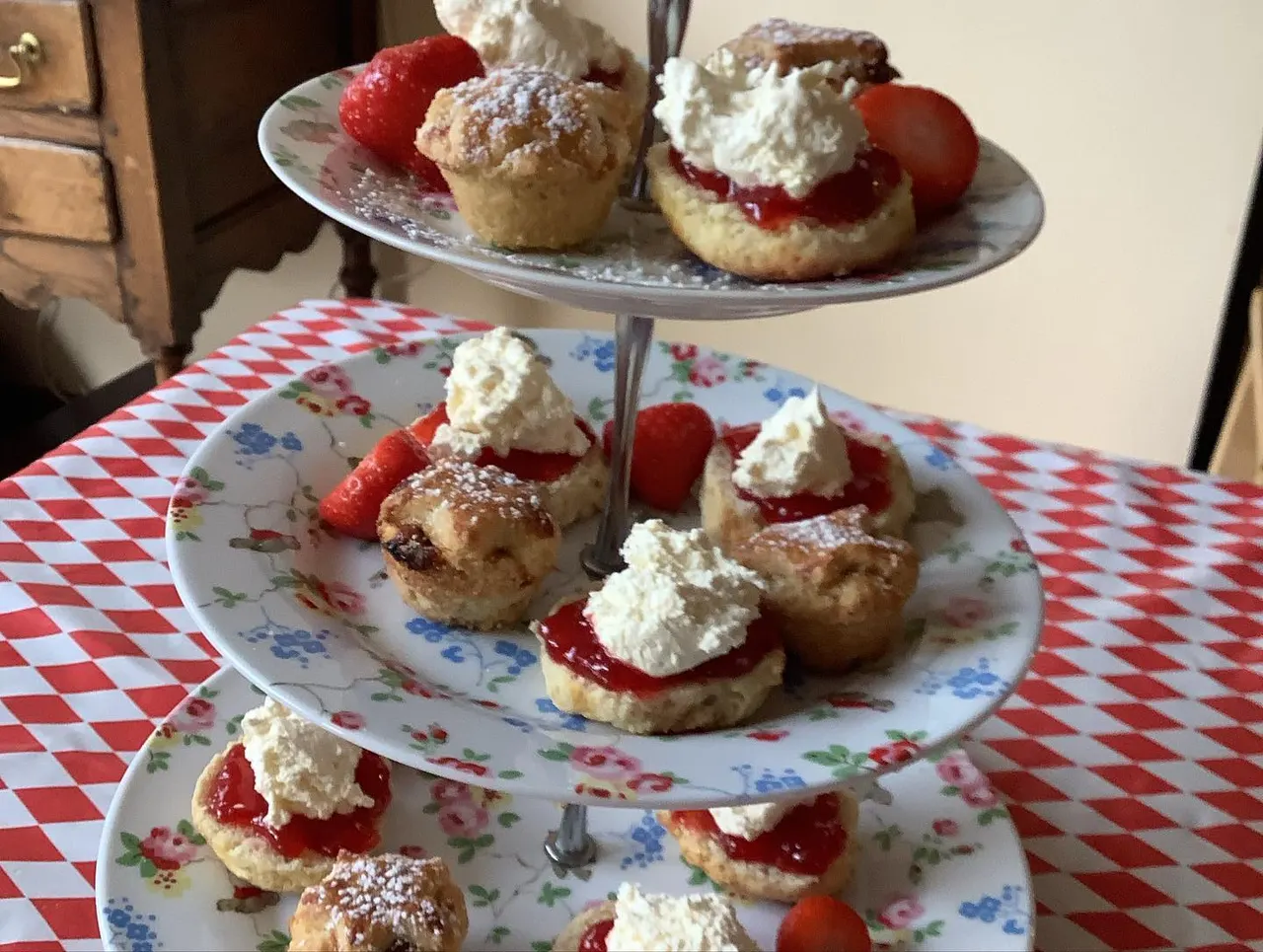 Three-tiered stand displaying cream teas with scones, jam, whipped cream and fresh strawberries on floral plates.