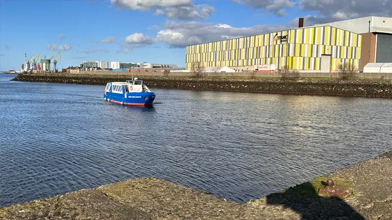 Blue and white tour boat on the water near a modern yellow-and-white building by the dockside.