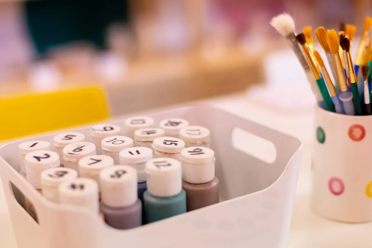 Numbered paint bottles and paintbrushes arranged on a craft table at an art activity venue.