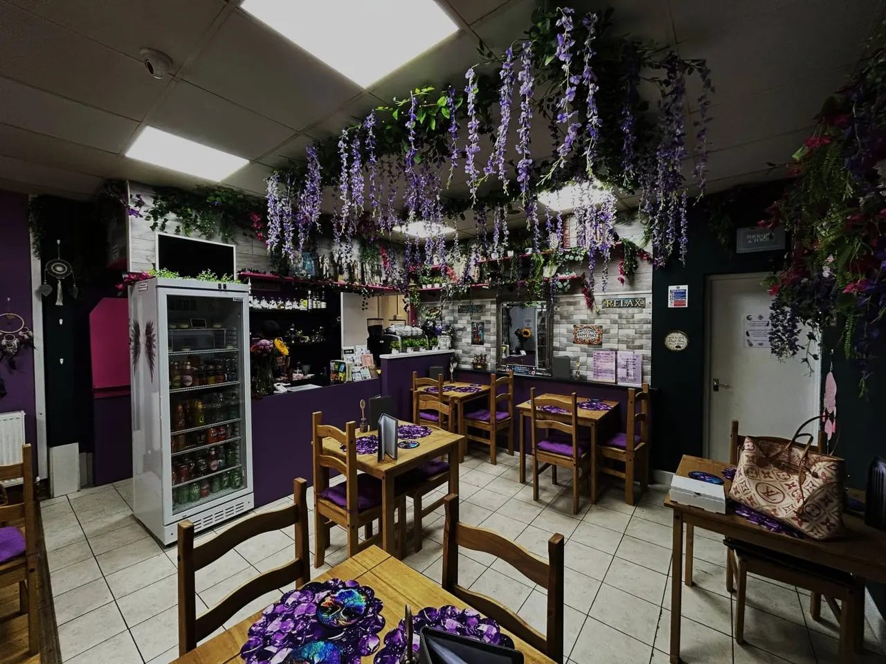 Interior of a café with wooden tables and chairs, decorated with cascading purple wisteria flowers hanging from the ceiling.