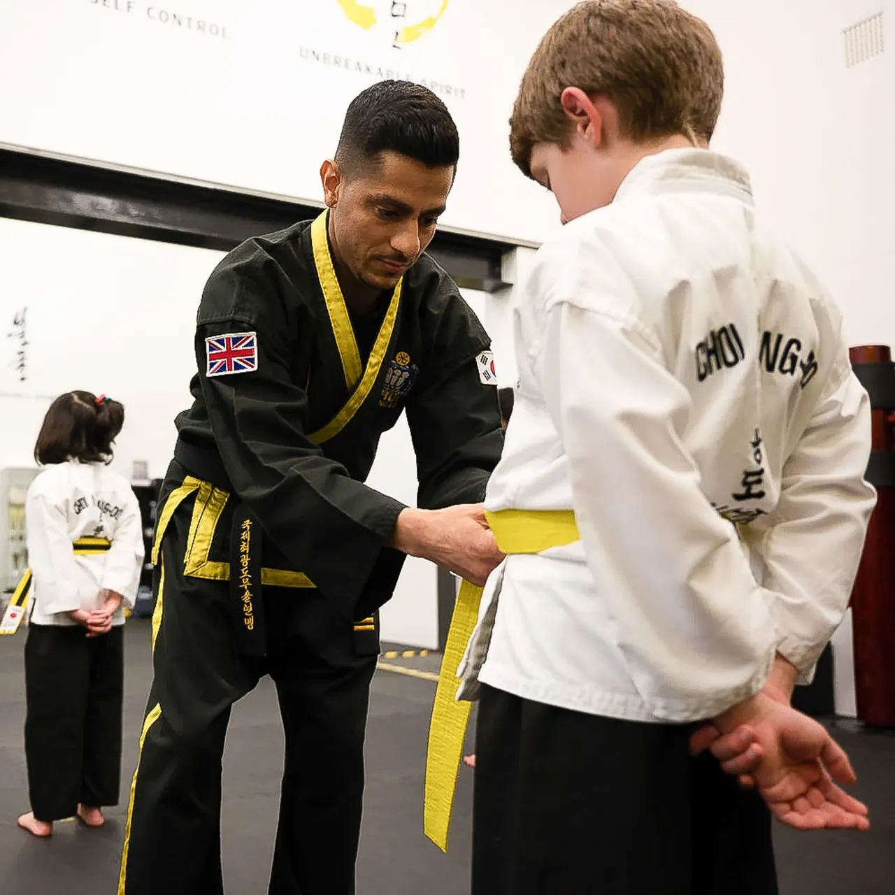 Martial arts instructor in black gi with yellow belt awarding a yellow belt to a young student in white gi.