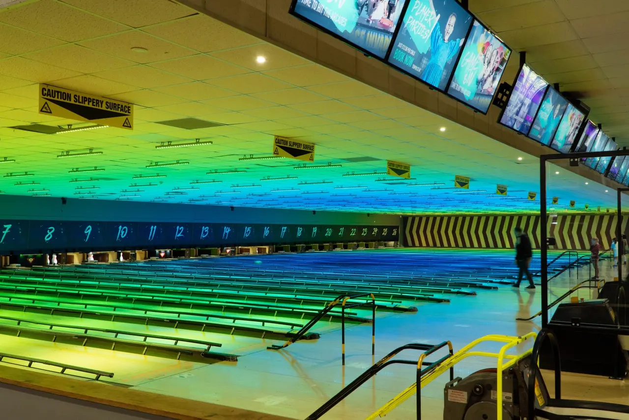 Empty bowling alley with colourful neon lighting illuminating multiple lanes and pins.