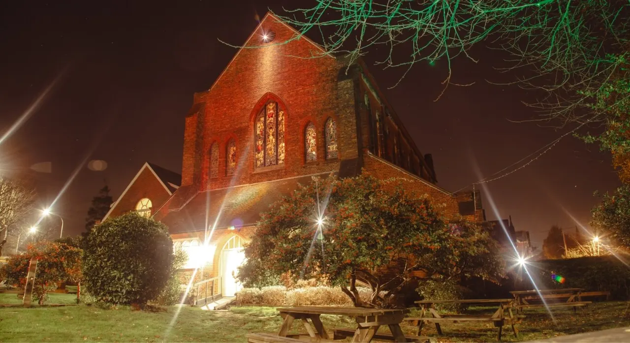 Red brick church building illuminated at night with picnic tables in the foreground.