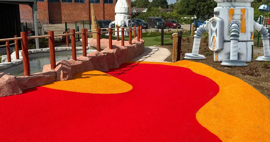 Colourful mini golf course with red and orange surface, wooden posts, and themed structures in a leisure venue car park.