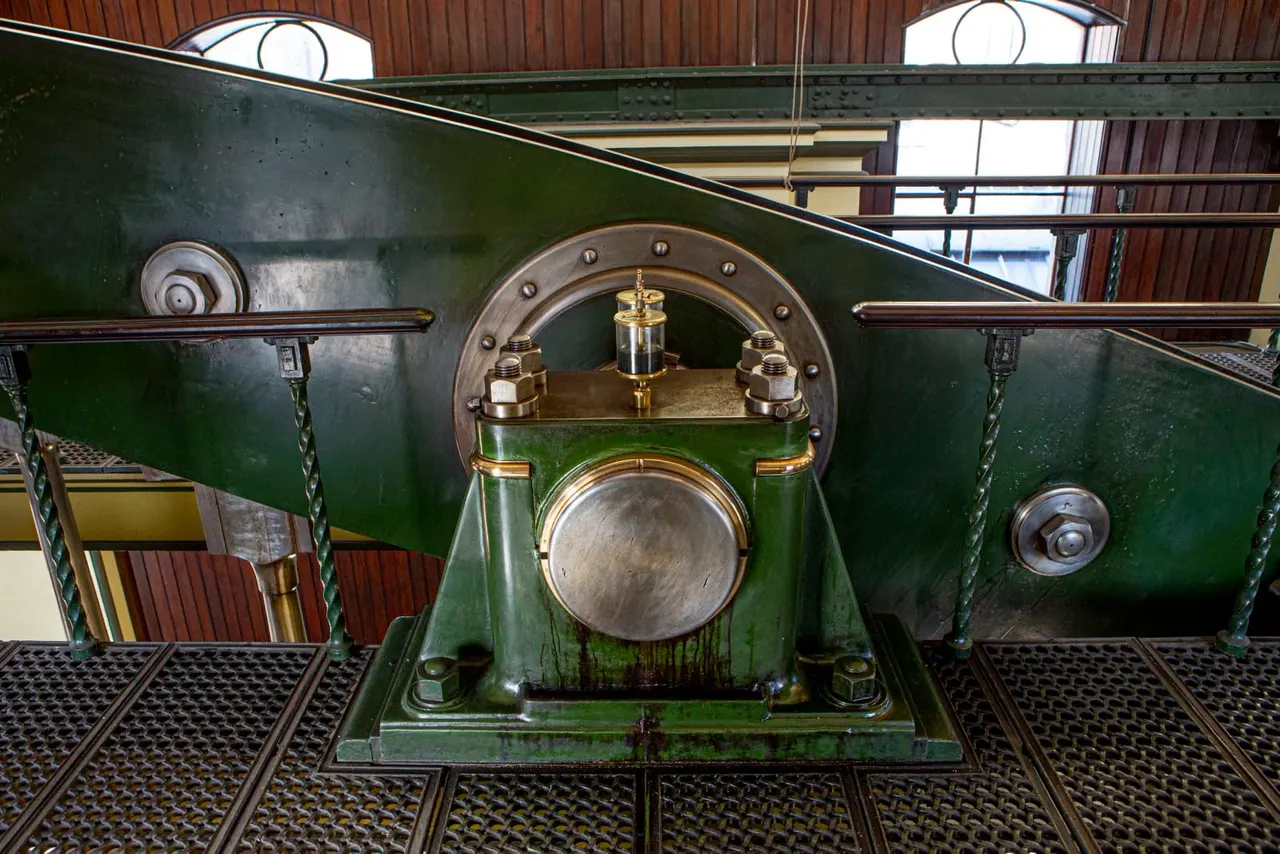 Close-up of a green vintage steam locomotive's front end showing brass fittings and circular details inside a heritage railway building.