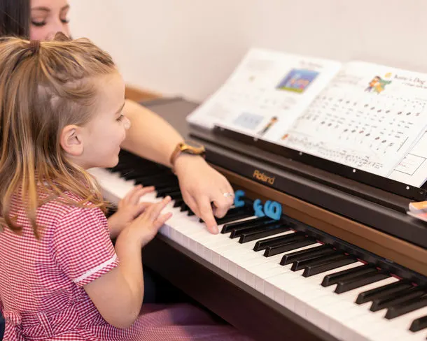 Young child in pink gingham dress playing electronic keyboard with sheet music on stand.
